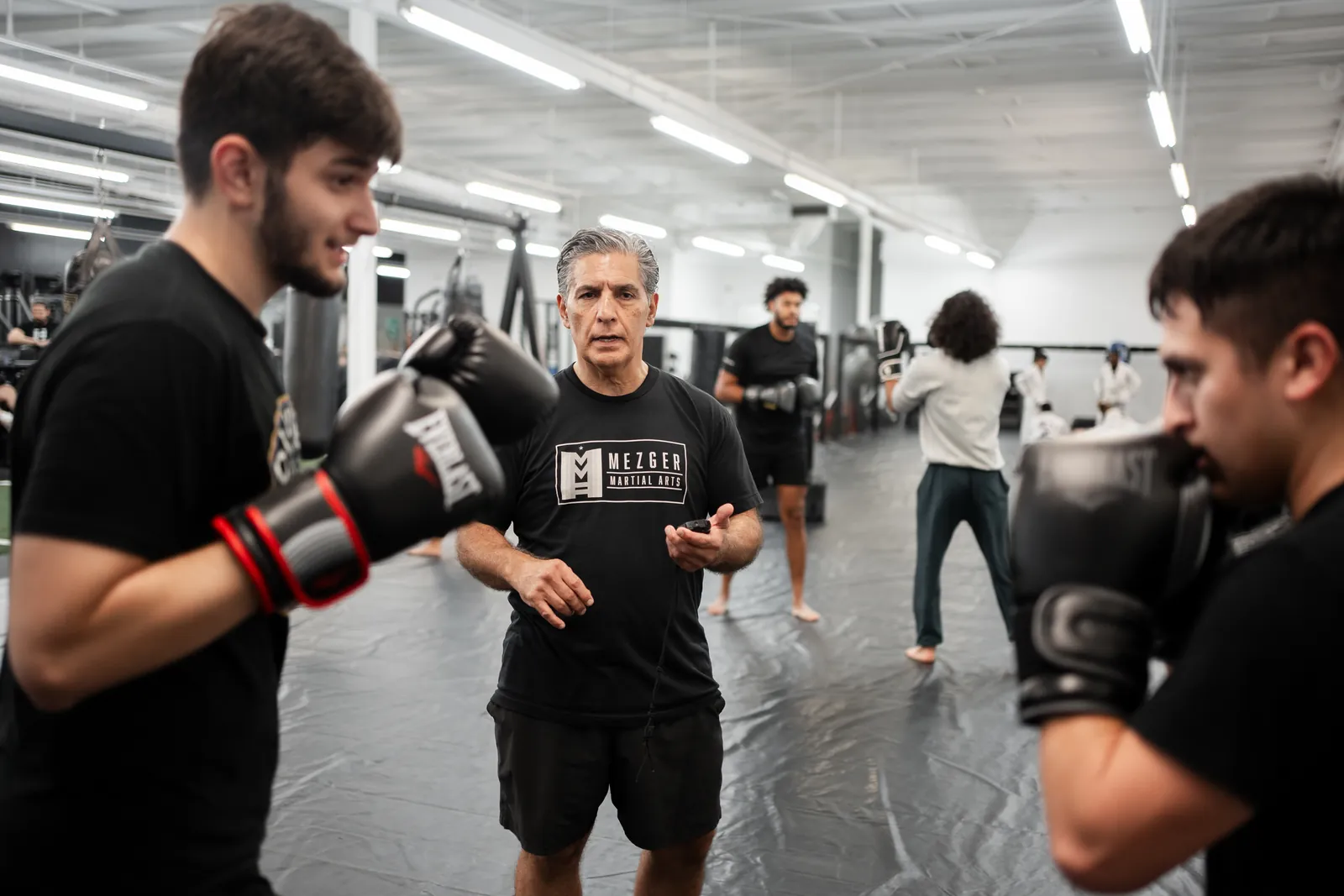 Guy Mezger coaching two students wearing boxing gloves on the mats at Hidden Gym Richardson