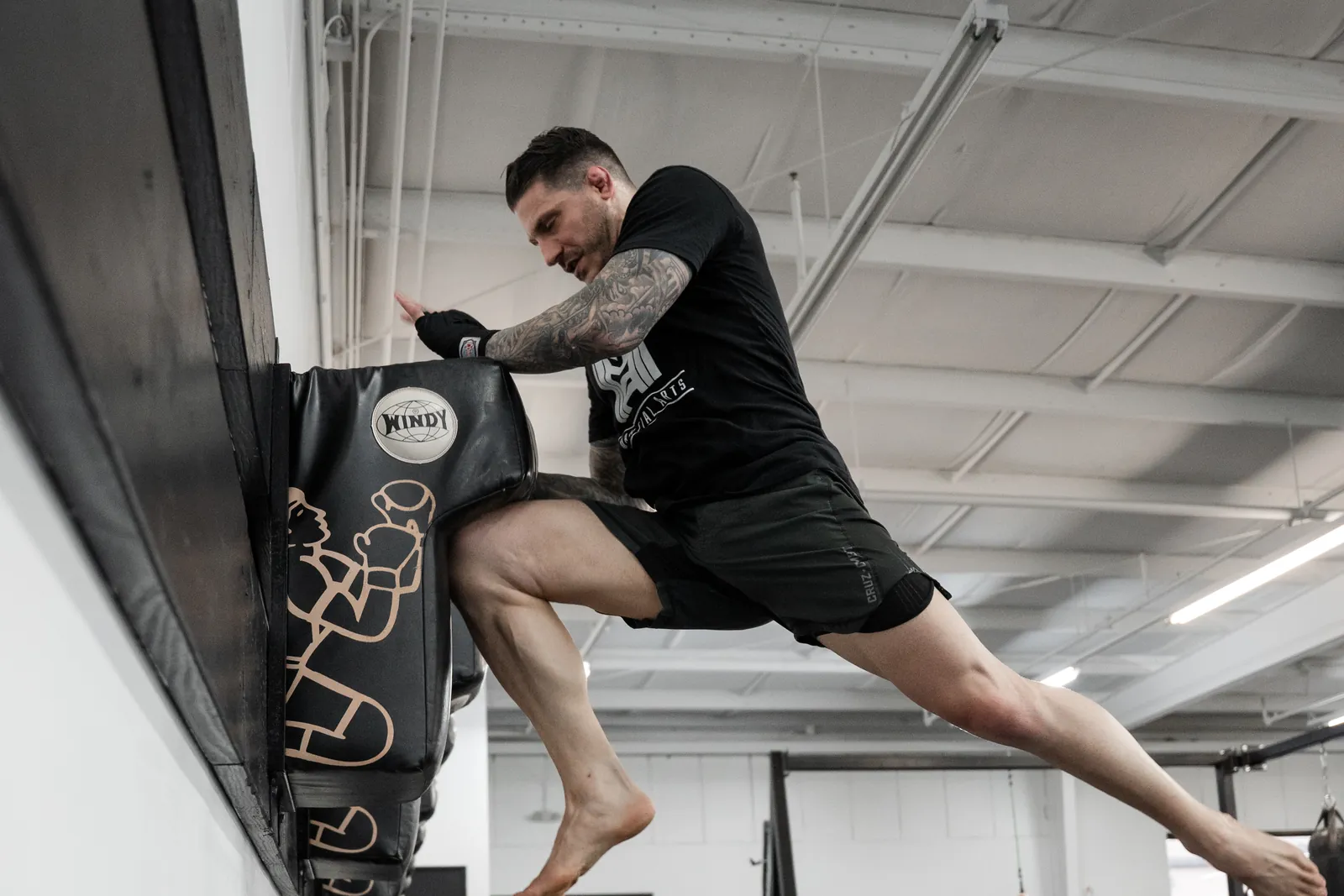 Fighter driving a flying knee into a heavy bag during kickboxing training at Hidden Gym
