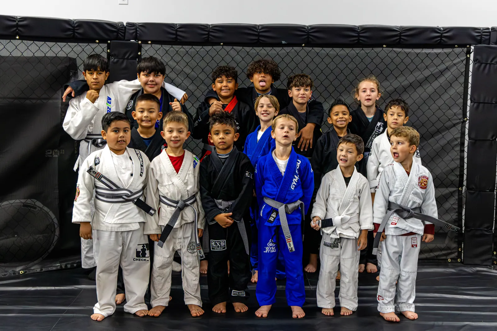 Group of kids in jiu-jitsu gis posing together inside the cage at Hidden Gym Richardson