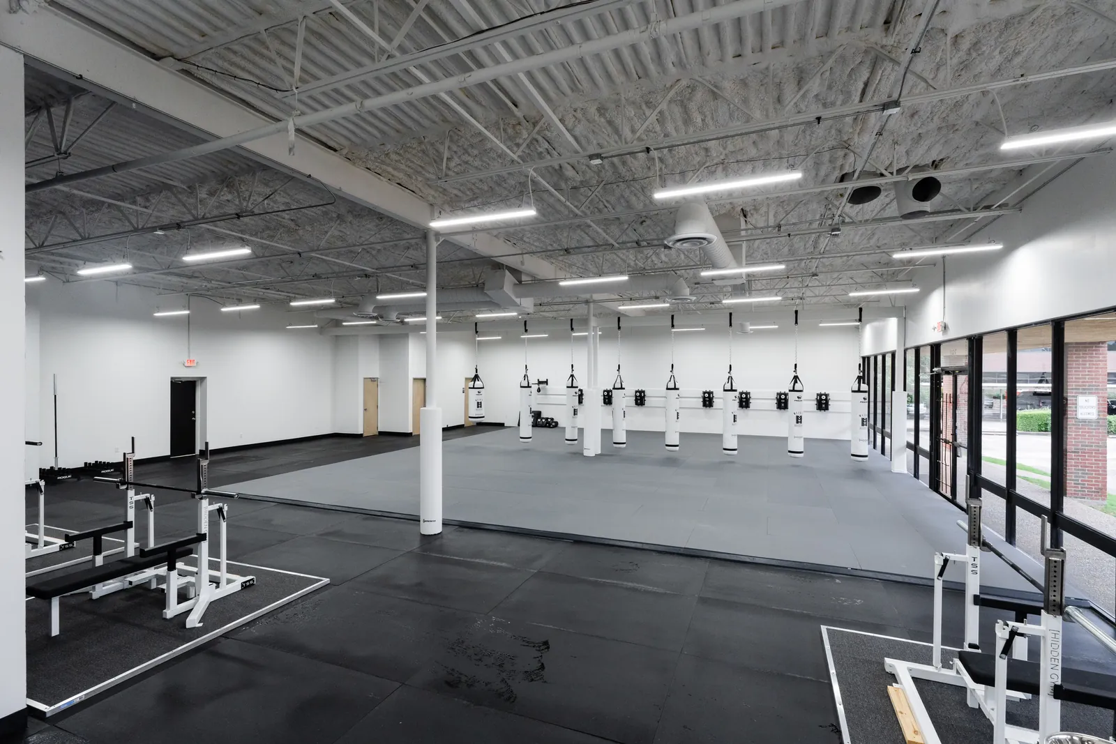 Dedicated martial arts room with grey combat mats and a row of heavy bags at Hidden Gym North Dallas