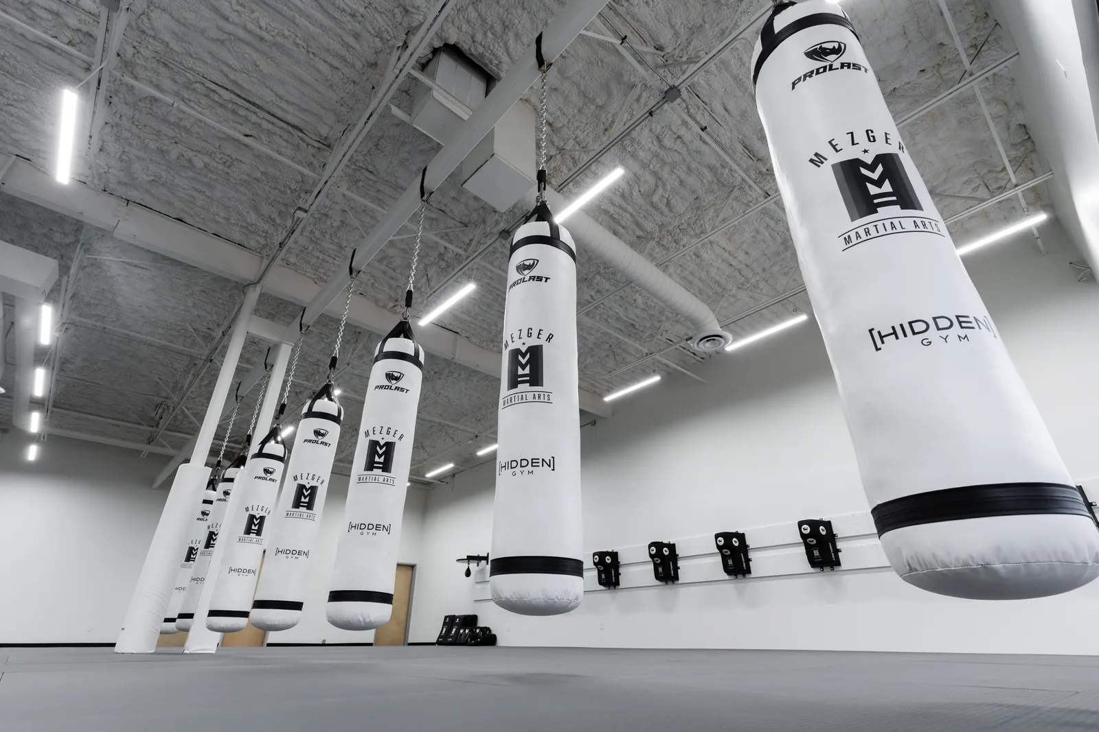 Row of Mezger Martial Arts branded heavy bags hanging in the martial arts room at Hidden Gym North Dallas
