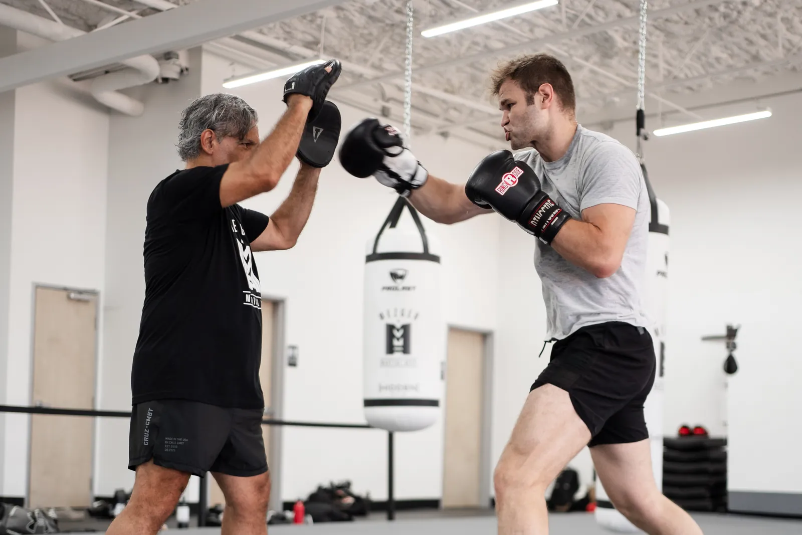 Coach holding focus mitts for a student in the martial arts room at Hidden Gym North Dallas
